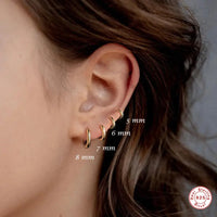 A person wearing a pair of silver hoop earrings, with the dimensions of the earrings labeled.