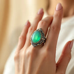 Lade Bild in die Galerieansicht, Color-changing mood ring with ornate filigree band showing teal-green stone worn on finger