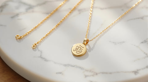 Delicate gold medallion pendant necklace with an abstract symbol relief next to thin gold chain necklaces on white marble, Awe Inspired goddess pendant inspired styling