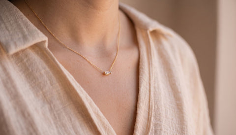 Woman wearing a delicate gold necklace with a small baguette-cut pendant