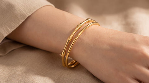 Gold bamboo-textured cuff bangle bracelet stacked with a smooth gold bangle on a wrist