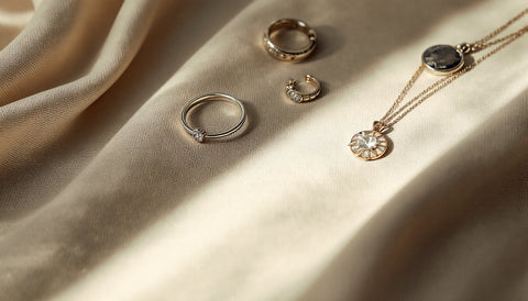 Flat lay of affordable sterling silver jewelry including rings, hoop earrings, and a pendant necklace on a neutral background