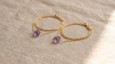 Two sterling silver charm necklaces with gemstone pendants laid flat on a neutral fabric surface