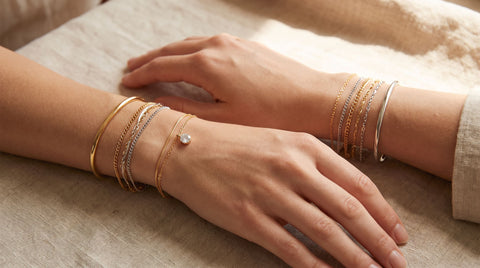 Two friends wearing matching stacked gold and silver bracelets on their wrists