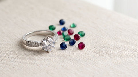 Sterling silver CZ solitaire engagement ring on cream linen beside loose colored gemstones