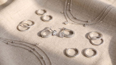 Flatlay of affordable sterling silver rings, hoop earrings, and layered necklaces on a neutral background