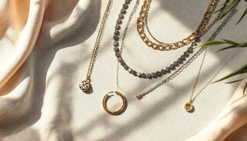Assorted trendy silver and gold jewelry including layered necklaces, hoops, and stacking rings arranged in a flat lay