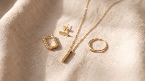 Flat-lay of minimalist gold and silver jewelry pieces including a thin necklace, small stud earrings, and a delicate ring