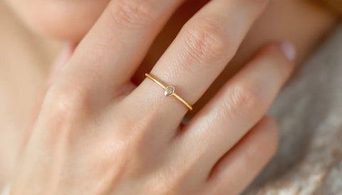 Hand wearing a thin gold stacking ring with an elongating oval stone, close-up styling shot