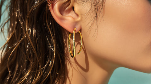 Woman wearing gold huggie hoop earrings with water droplets on skin, waterproof earrings styling shot