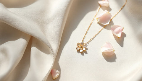 Delicate gold birth flower pendant necklace styled flat lay with flower petals