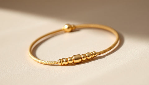 A gold bolo bracelet with sliding adjustable mechanism displayed on a neutral surface