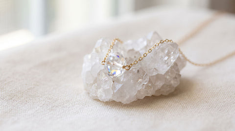 Clear quartz crystal charm necklace resting beside a raw clear quartz crystal point