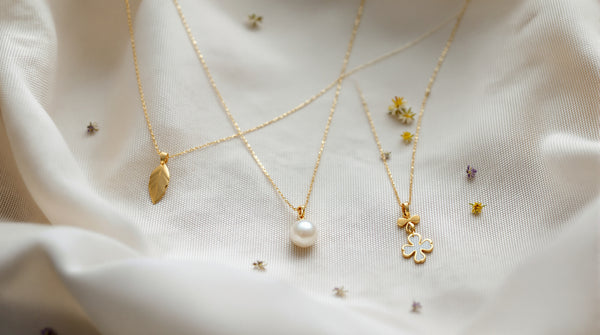 Delicate freshwater pearl necklace styled with a gold leaf charm and clover pendant on linen with dried wildflowers, cottagecore jewelry aesthetic flat lay