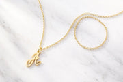 Dainty gold necklace with heart initial pendant on white marble surface, AJLuxe personalized jewelry