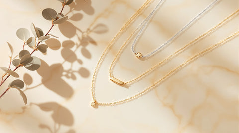 Dainty layered necklaces flat lay - three fine 18K gold and sterling silver chains at staggered lengths on cream marble