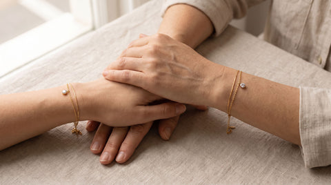 Mother and daughter's hands overlapping, each wearing a delicate adjustable gold bracelet