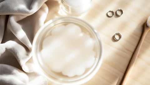 Homemade jewelry cleaning setup with soapy water, a soft cloth, and silver rings on a wooden surface