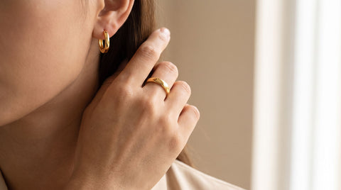 Close-up of gold-plated sterling silver hoop earrings and a ring worn on hand, showing everyday jewelry against skin