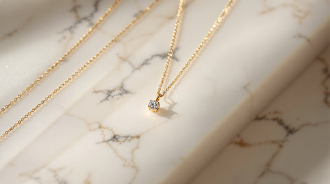 Delicate gold pendant necklace with a single round CZ stone next to thin gold chain necklaces on white marble, Dorsey floating necklace inspired styling