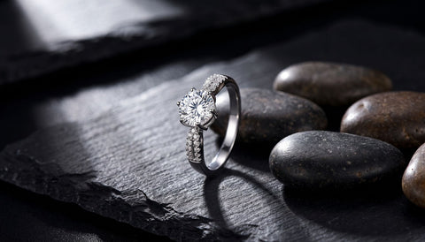Unplated sterling silver cubic zirconia ring standing on dark slate beside smooth river pebbles