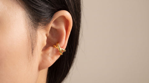 Gold ear cuff worn on the cartilage of a woman's ear, showing the no-piercing grip that differs from a clip-on earring's lobe clip