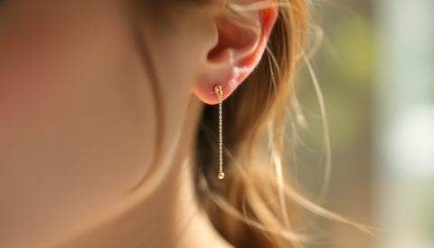 Delicate gold stud earring with a fine chain draping from the front of the ear to behind the lobe