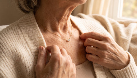 Close-up of an elderly woman wearing a delicate gold necklace with a small baguette birthstone pendant at her collarbone