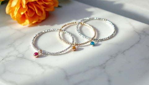 Silver charm bracelets with colorful bead charms laid side by side on white marble, comparing Gnoce and Pandora style charm jewelry