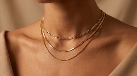 Layered gold chain necklaces including curb, snake, and box chains worn together