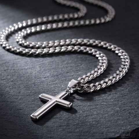 Men's cuban link chain with a polished cross pendant laid across dark slate