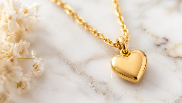Close-up of 18K gold plated heart initial necklace on white marble, showing gold finish and warm tone
