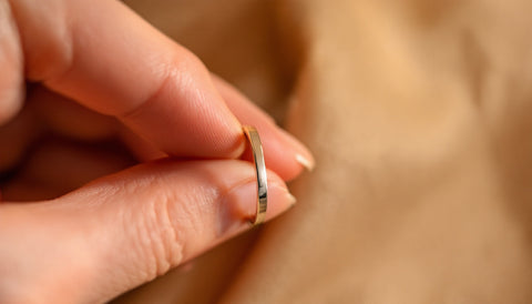 Close-up macro product photography of a slim sterling silver ring being gently slid onto a woman's finger past the knuckle