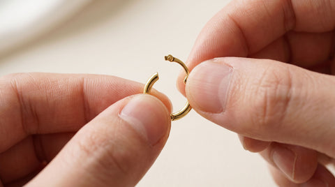 Hands gently opening a gold huggie hoop earring at its hinge