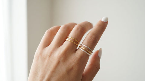 Hand wearing a stack of gold and silver rings across two fingers