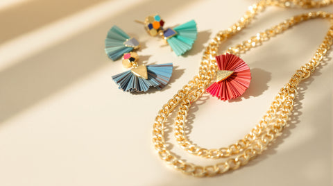 Colorful statement earrings and a layered gold necklace arranged on a clean light surface