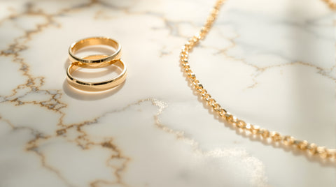 Macro photograph of gold-plated rings and a necklace showing the warm gold surface layer over a metal base, on white marble