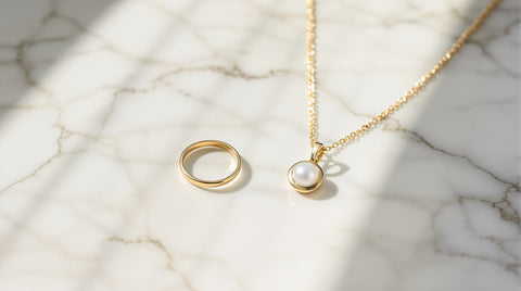 Delicate 18K gold vermeil style ring and pendant necklace on a sterling silver base resting on white marble in warm natural light