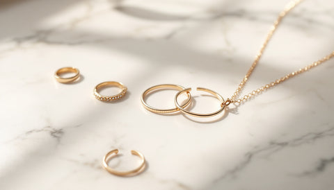 Minimalist gold and silver stacking rings, hoops, and a pendant necklace arranged on a marble surface