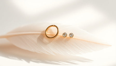 Tiny gold huggie hoop and stud earrings resting on a pale feather