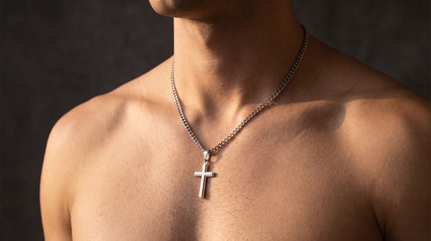 Silver cuban link cross necklace worn at the collarbone on a man's bare chest