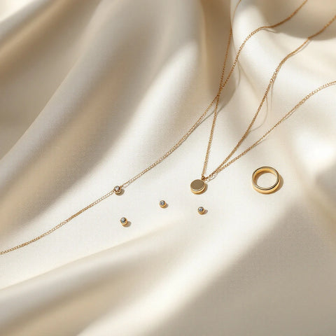 A curated flat-lay of minimalist jewelry: dainty chain necklace, petite studs, thin hoops and a slim ring
