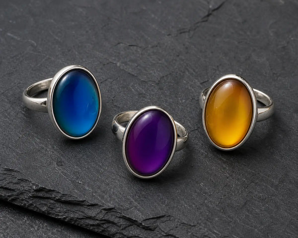 Three mood rings showing different colours — blue, purple, and amber — on a dark surface, illustrating how mood ring colours change with body temperature