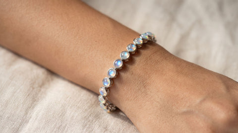 Bezel-set rainbow moonstone tennis bracelet on a stainless steel band, worn on a wrist