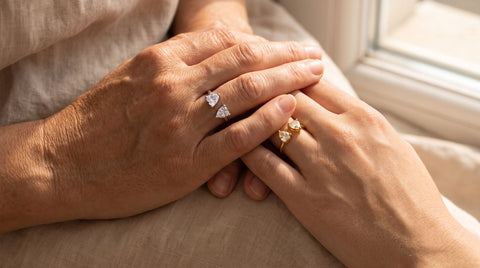 Mother's and daughter's hands wearing matching adjustable heart rings, one silver one gold