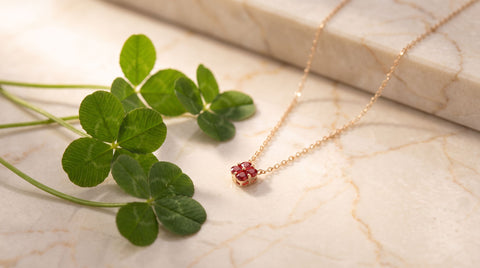 Sterling silver four-leaf clover pendant necklace resting on a marble surface next to real clover leaves