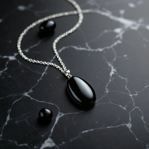 Black obsidian pendant necklace on dark marble showing glassy reflective surface — obsidian meaning guide