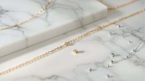 Delicate 18K gold-plated CZ chain bracelet on white marble beside thin gold chains and loose silver charms, Pandora charm bracelet inspired styling