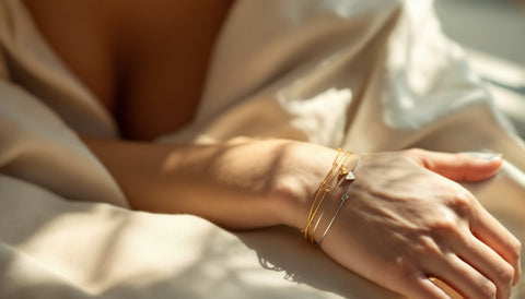 Woman's wrist wearing a personalized gold-plated heart charm bracelet stacked with thin silver bangles