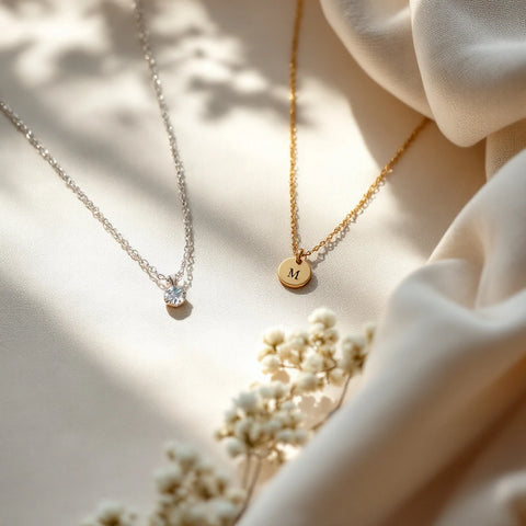 Push present jewelry — dainty personalized birthstone and initial necklaces on soft neutral fabric with a folded baby swaddle